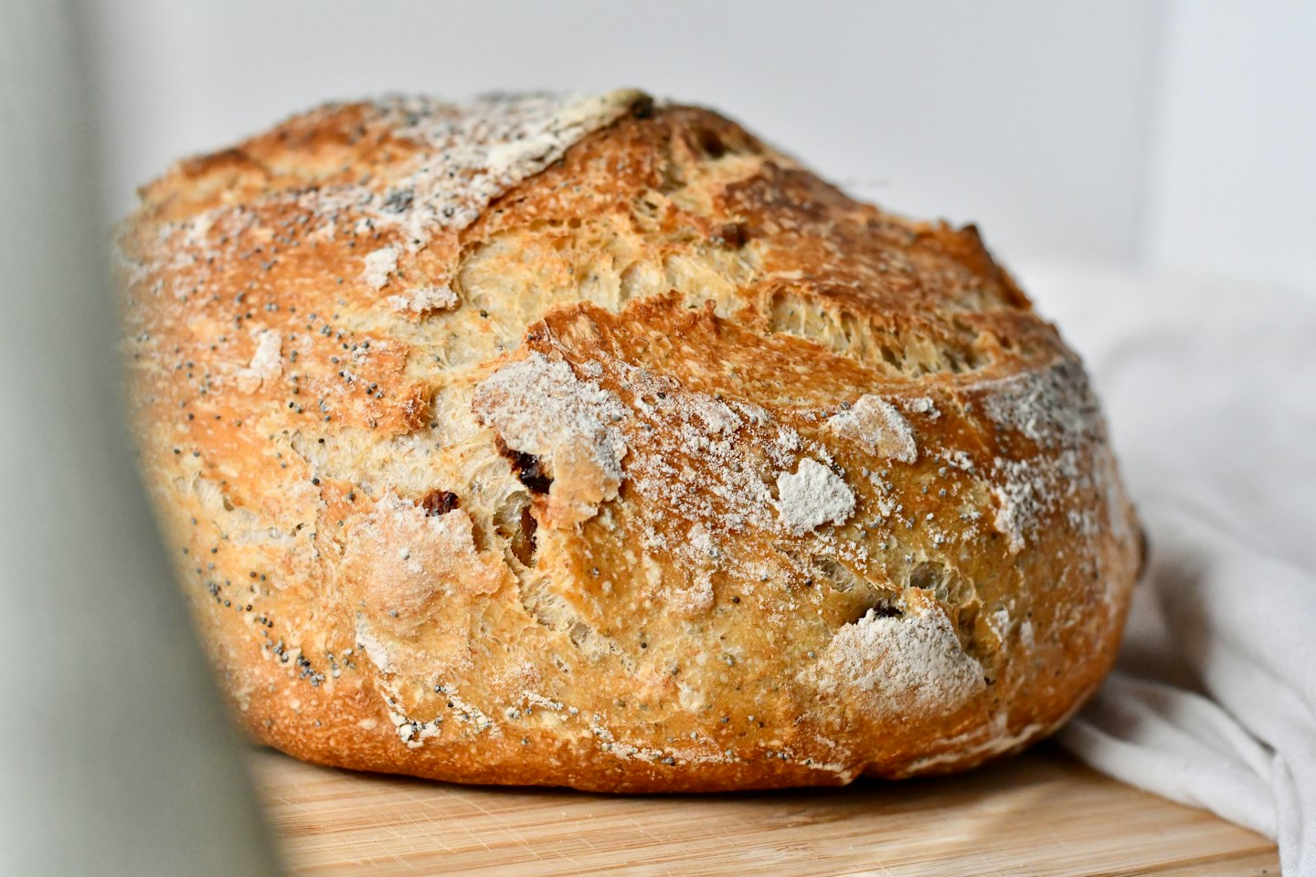 A crusty sourdough loaf with poppy seeds on a board.