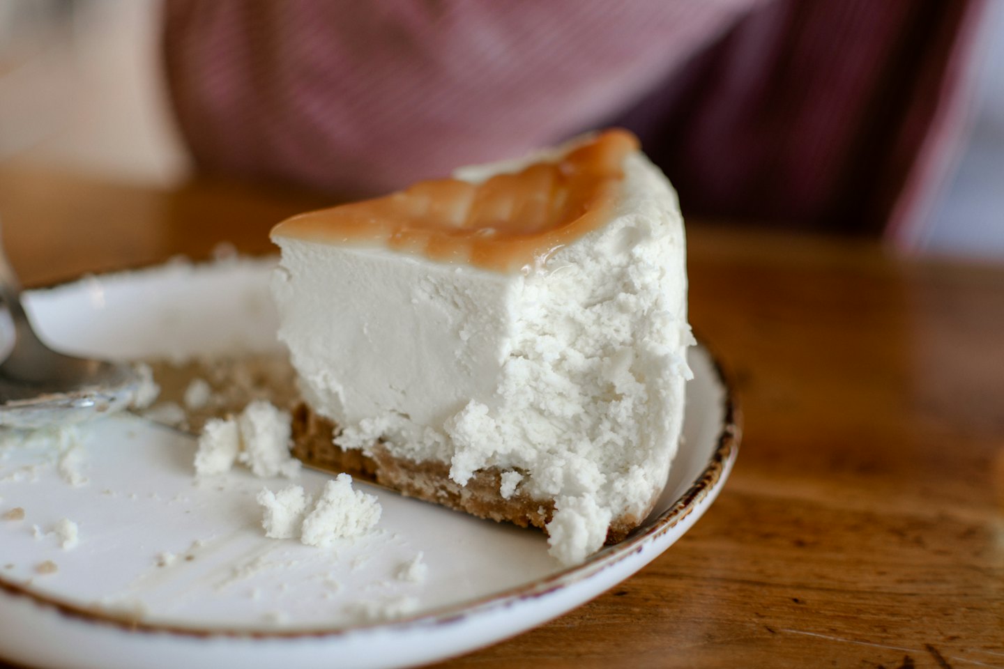 A slice of cheesecake with caramel sits on a plate.
