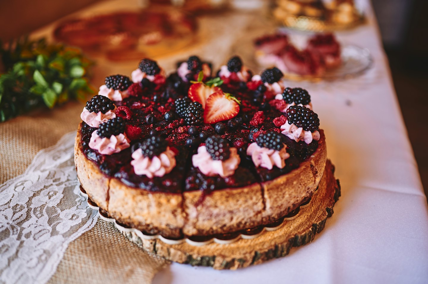 Berry cheesecake decorated with fruit sits on a wooden stand.